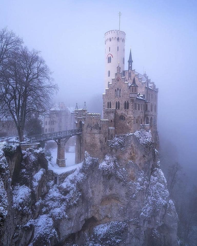 A castle perched on a snowy cliff surrounded by fog.